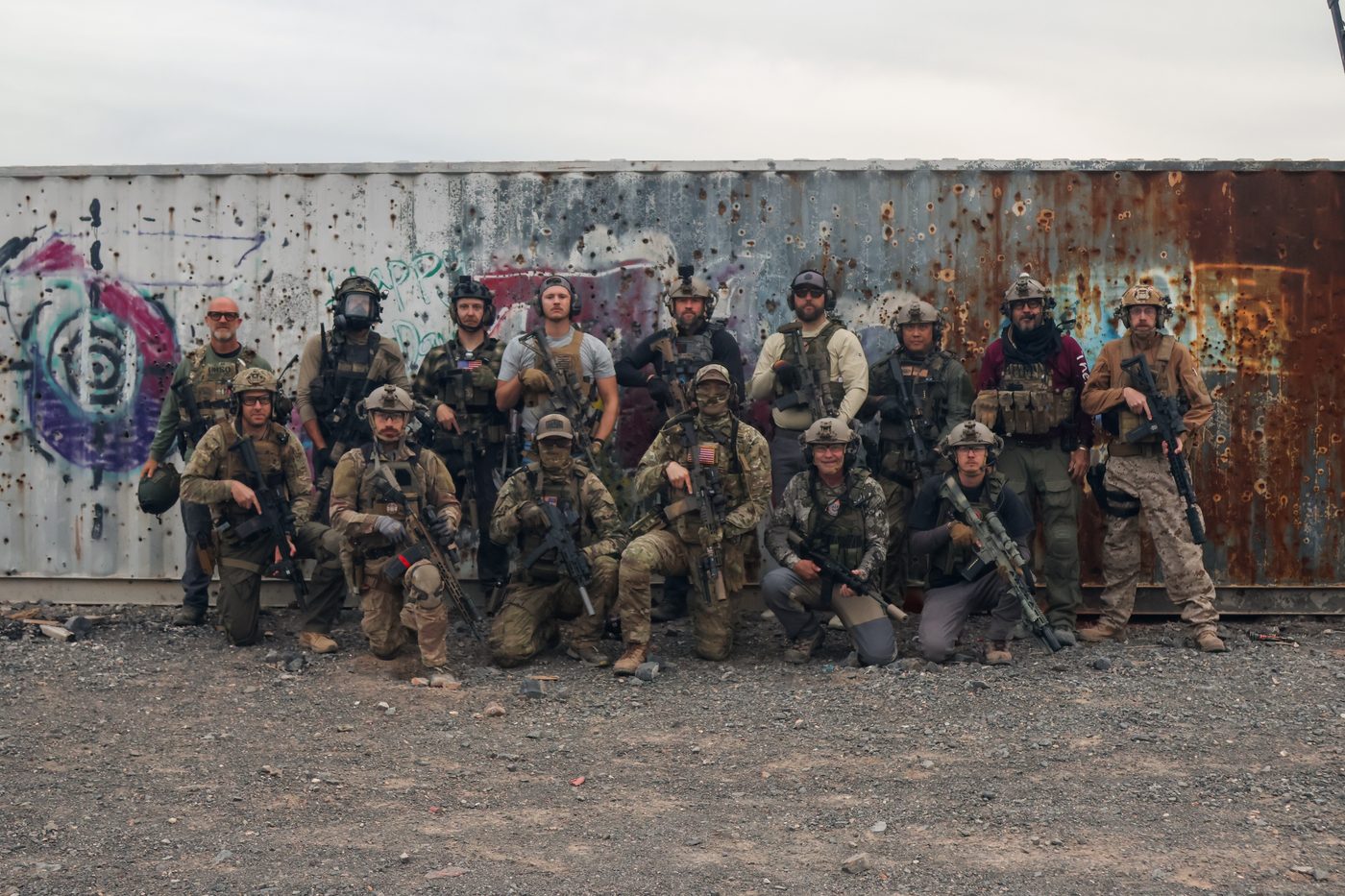 The Art Room trainees posing with rifles by a shipping container