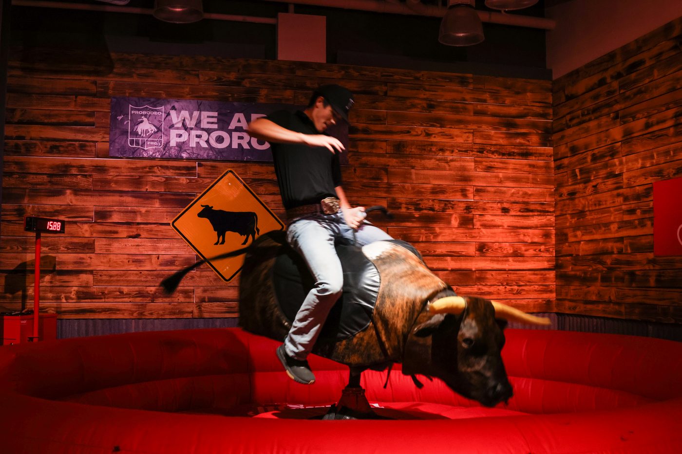A rider on the mechanical bull at an indoor venue with a scoreboard timer