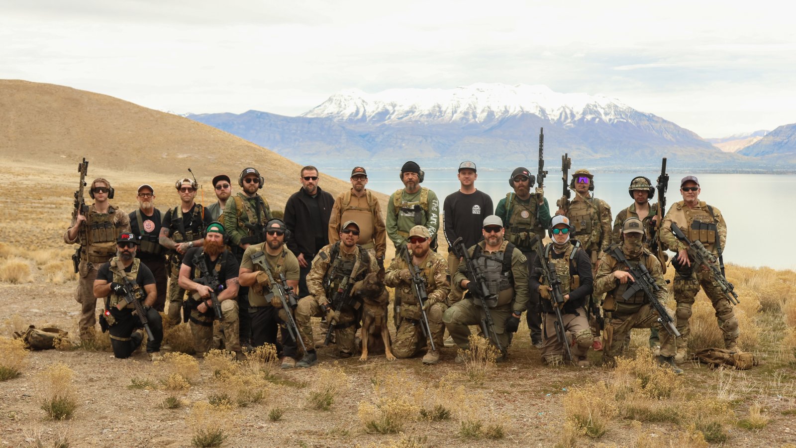 A group of The Art Room trainees posing with rifles in front of a mountain lake