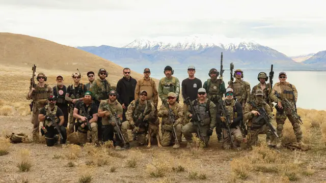A group of The Art Room trainees posing with rifles in front of a mountain lake